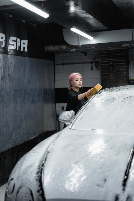 A woman cleaning her car with foam and sponge in an indoor car spa setting.