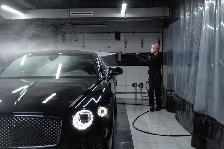 A woman using a power spray to wash a luxury car inside a garage, emphasizing precision and care.
